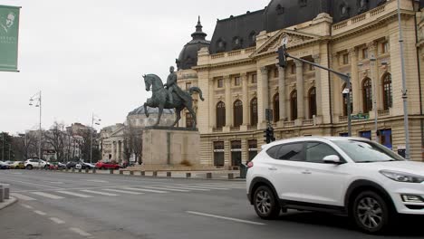 White-car-drives-in-front-of-the-historic-Bucharest-library-with-a-bronze-equestrian-Carol-I-of-Romania-statue