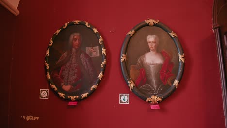 Retratos-Ornamentados-De-Personajes-Históricos-Exhibidos-En-Marcos-Dorados-Contra-Un-Fondo-Rojo-Vibrante-En-El-Castillo-De-Trakošćan,-Croacia