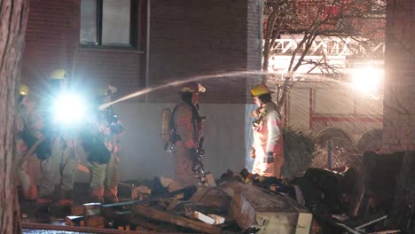 A-team-of-firefighters-at-the-scene-of-a-residential-building-fire-at-night,-extinguishing-the-flames-on-the-damaged-property-that-remains-from-the-devastating-blaze