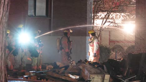 Un-Equipo-De-Bomberos-En-El-Lugar-Del-Incendio-De-Un-Edificio-Residencial-Por-La-Noche,-Extinguiendo-Las-Llamas-En-La-Propiedad-Dañada-Que-Queda-Del-Devastador-Incendio.