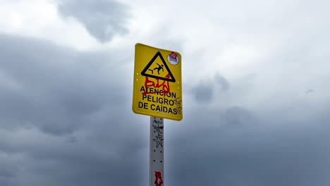 grafitti-on-spanish-public-warning-sign-next-to-the-sea,-cloudy-sky