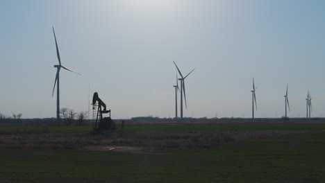 Oklahoma---Oil-pumpjack-Silhouette-with-Row-of-Wind-Turbines-in-Backround