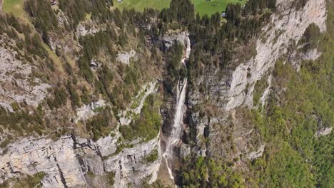 A-dramatic-waterfall-cascading-through-rugged-cliffs-in-a-lush-green-valley,-shot-during-the-day,-aerial-view