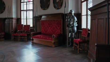 Regal-sitting-area-with-a-red-upholstered-bench-and-suit-of-armor,-under-historic-portraits-in-Trakoscan-Castle's-Chivalric-Hall