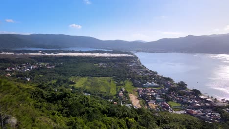 Aerial-drone-view-of-man-on-top-of-mountain-revealing-skyline-with-lagoon-and-ocean-amid-city