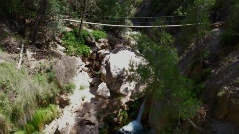 Hängender-Holzsteg-über-Einem-Gebirgsbach-Und-Einem-Wasserfall-Mit-Farbenfrohem,-Türkisfarbenem-Wasser