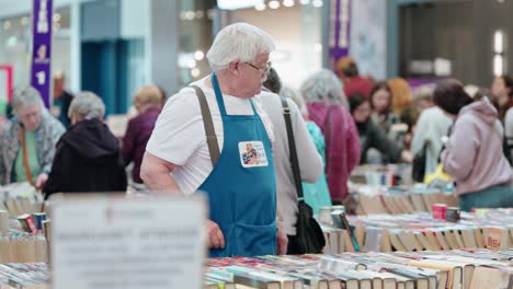 Ein-Alter-Mann-Mit-Weißem-Haar-Organisiert-Bücher-Aus-Der-Bibliothek-Bei-Einem-Verkauf-Gebrauchter-Romane-In-Einem-Einkaufszentrum