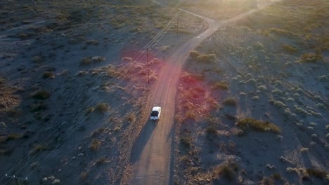 Aerial-view-drone-of-white-van-driving-through-desert-road-at-sunset