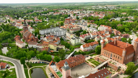 Una-Toma-Aérea-Más-Amplia-De-Lidzbark-Warmiński-Que-Muestra-El-Diseño-De-La-Ciudad-Con-Edificios-Históricos-Y-Modernos,-Espacios-Verdes-Y-La-Destacada-Iglesia.