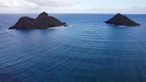 In-Dieser-Drohnenaufnahme-Brechen-Sich-Die-Blauen-Meereswellen-Um-Die-Kleinen-Inseln,-Die-Aus-Der-Meeresoberfläche-In-Der-Nähe-Von-Oahu,-Hawaii,-Am-Strand-Von-Lanikai-Herausragen.