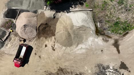 Drone-top-down-pan-across-empty-dump-trucks-parked-by-dirt-stockpile