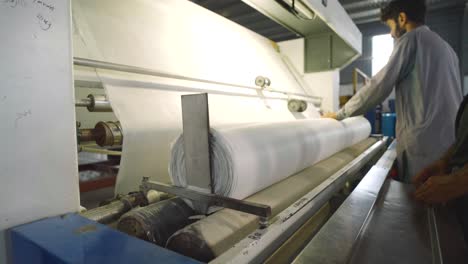 Large-White-Fabric-Being-Rolled-By-Machine-Tended-To-By-Worker-In-Textile-Factory