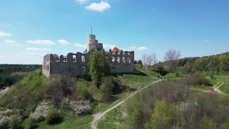 Medieval-Rabsztyn-castle-with-a-turret,-walls,-and-courtyard-during-a-beautiful-summer-day-surrounded-by-lush-greenery,-grass,-and-trees-under-a-clear-blue-sky