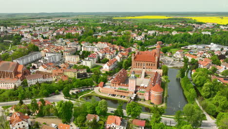 Una-Amplia-Vista-Aérea-De-Lidzbark-Warmiński,-Que-Muestra-La-Combinación-De-Arquitectura-Histórica-Y-Moderna-De-La-Ciudad,-áreas-Verdes-Y-Un-Importante-Edificio-Histórico-Cerca-De-Un-Cuerpo-De-Agua.