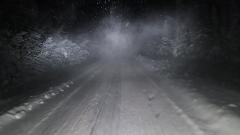 POV-shot-of-a-logistics-truck-passing-a-vehicle-on-a-dark-snow-covered-icy-road,-the-vehicle-kicking-up-a-trail-of-snow-dust-obscuring-visibility-as-the-driver-switches-on-his-high-beam-headlights