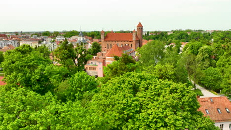 A-closer-aerial-view-of-Lidzbark-Warmiński,-highlighting-a-prominent-historical-building-with-red-rooftops-surrounded-by-green-trees-and-urban-structures