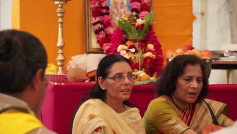 Two-Hindu-women-chant-with-religious-icons-behind-them-honoring-the-deity,-Ganesh