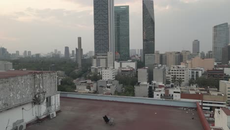 Persona-Sentada-En-Una-Azotea,-Admirando-Los-Rascacielos-De-La-Ciudad-De-México-Mientras-Un-Dron-Se-Aleja-Volando