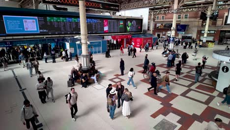 Busy-day-at-London-Victoria-Station-with-people-walking,-waiting,-and-checking-the-train-schedule-on-the-concourse