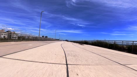 Low-angle-view-of-an-FPV-drone-flying-fast-and-low-over-an-empty-beach-boardwalk-on-a-sunny-day-with-blue-skies