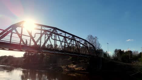Drone-Fly-above-river-contrasted-metallic-bridge-crossing-water-sunshine-skyline