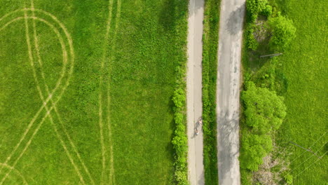 An-aerial-view-of-a-rural-road-with-two-bikers-riding-along-it,-surrounded-by-green-fields