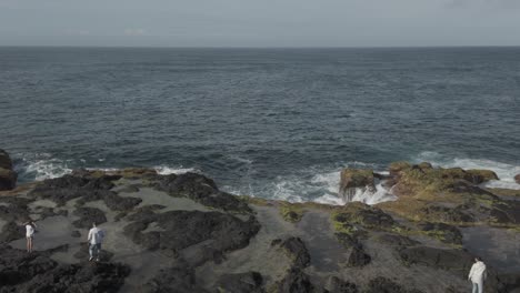 Couple-explores-the-rugged-coastline-of-Mosteiros,-Sao-Miguel-in-the-Azores-with-volcanic-rocks-and-crashing-waves