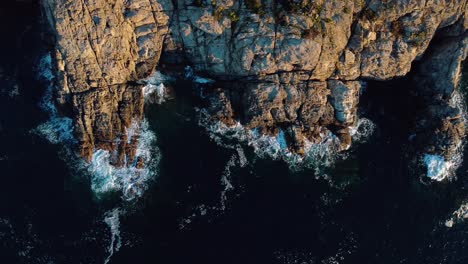 Impresionante-Vista-Aérea-De-Las-Olas-Rompiendo-Contra-Las-Rocas,-Resaltando-Los-Contrastes-De-Colores-Naturales-Y-Las-Texturas-Que-Evocan-El-Poder-Y-La-Belleza-De-La-Naturaleza-En-Su-Máxima-Expresión.