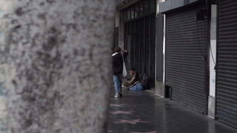 Los-Angeles-USA,-Homeless-Man-Sitting-by-the-Building-on-Walk-of-Fame-Sidewalk-of-Hollywood-Boulevard,-Slow-Motion