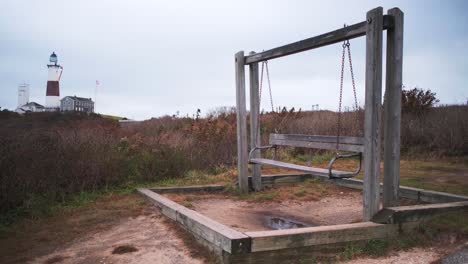 Schwingende-Leere-Holzschaukel-Im-Vordergrund-Und-Der-Montauk-Leuchtturm-Im-Hintergrund