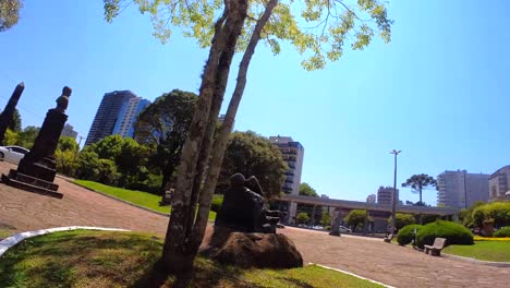 Orbital-view-of-Negrinho-do-Pastoreio-Statue,-local-Brazilian-legend-about-black-slavery-and-history-under-a-sunny-day-with-blue-sky