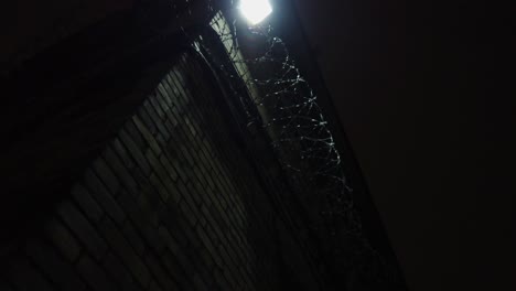 Dark-abandoned-prison-yard,-sharp-fences-visible-at-night,-the-outside-lamp-is-shining