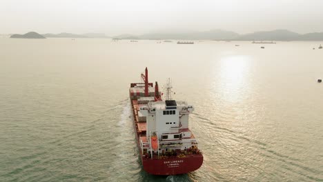 Mega-Container-Ship-leaving-Hong-Kong-port-at-sunset,-aerial-view