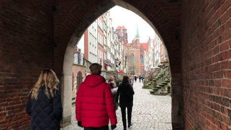 Looking-towards-St-May's-Basilica-from-medieval-archway-along-a-cobbled-street-called-Mariacka,-Gdansk,-Poland-on-a-cold-Winter's-day-with-tourists-walking-about