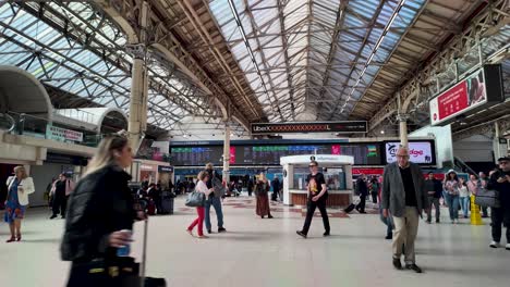Belebte-Bahnhofshalle-Im-Bahnhof-London-Victoria-Mit-Menschen,-Die-In-Verschiedene-Richtungen-Unter-Einem-Glasdach-Und-Informationstafeln-Gehen