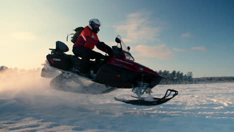 Hombre-En-Una-Moto-De-Nieve-Saltando-Sobre-Un-Lago-Nevado-Un-Soleado-Día-De-Invierno,-Primer-Plano