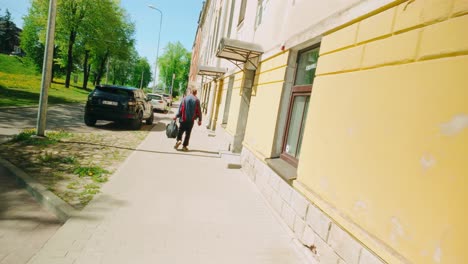 Drunk-man-walking-on-bright-and-sunny-street-carrying-a-plastic-bag-Dutch-angle-pov-rear-view