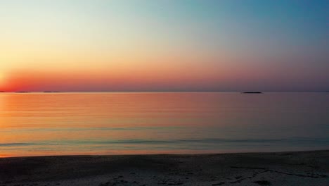 Schwenkansicht-Von-Rechts-Auf-Den-Herrlichen-Sonnenaufgang-Am-Strand-Mit-Hell-Leuchtender-Sonne,-Die-Farbenfrohe-Rot-orange-violette-Und-Gelbe-Spiegelbilder-über-Friedlich-Plätschernde-Wellen-Des-Meeres-Mit-Wunderschönem-Himmel-Und-Meerwasser-Wirft