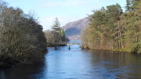 Scenic-view-of-idyllic-wooden-bridge-over-River-Oich-into-Loch-Ness-from-Fort-Augustus-in-the-highlands-of-Scotland-UK