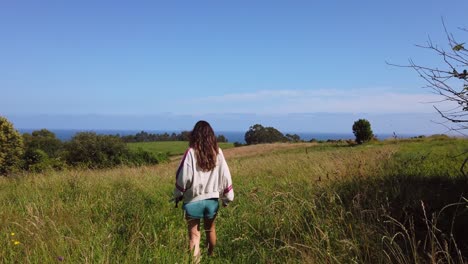 Junges-Spanisches-Brünettes-Mädchen-In-Shorts,-Das-In-Zeitlupe-Rückwärts-Auf-Einem-Grünen-Naturfeld-Läuft