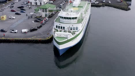 Ferry-Herjolfur-docking-at-Vestmannaeyjar-harbor-to-unload-passengers,-aerial