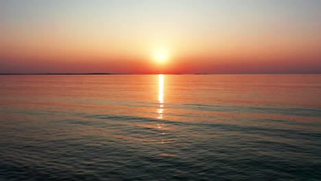 Wunderschöner-Sonnenaufgang-Am-Strand-Mit-Hell-Leuchtender-Sonne,-Die-Farbenfrohe-Rote,-Orange,-Violette-Und-Gelbe-Reflexe-Auf-Die-Friedlich-Plätschernden-Wellen-Des-Meeres-Wirft