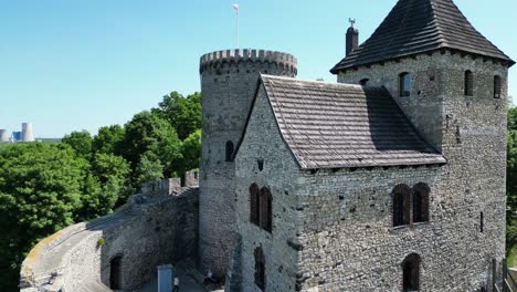 Medieval-Bedzin-castle-with-a-turret,-stone-walls,-and-courtyard-during-a-beautiful-summer-day-surrounded-by-lush-greenery,-under-a-clear-blue-sky