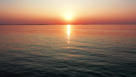 Aerial-Drone-View-of-Gorgeous-Ocean-Sunset-with-Bright-Glowing-Sun-Casting-Colorful-Red,-Orange,-Purple-and-Yellow-Reflections-Over-Peaceful-Rippling-Waves-of-the-Sea-with-Beautiful-Sky-and-Water