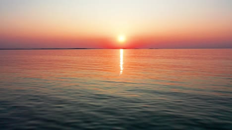 Aerial-Drone-View-of-Beautiful-Ocean-Sunset-with-Bright-Glowing-Sun-Casting-Colorful-Red,-Orange,-Purple-and-Yellow-Reflections-Over-Peaceful-Rippling-Waves-of-the-Sea-with-Gorgeous-Sky-and-Water