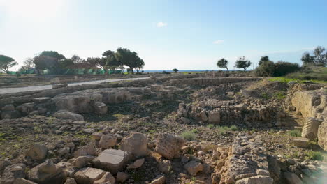 Una-Vista-Del-Sitio-Arqueológico-En-Chipre-Con-Antiguas-Ruinas-De-Piedra-Con-Un-Telón-De-Fondo-De-árboles-Y-El-Mar.