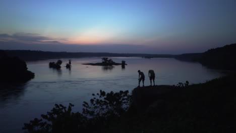 Men-with-head-lamp-at-dusk,-walking-and-sitting-on-the-bank-of-the-river-Nile-near-Jinja-Uganda