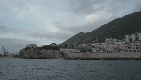 Eine-4k-Aufnahme-Bei-Sonnenuntergang-An-Einem-Dunklen-Und-Bewölkten-Tag,-Von-Einer-Drohne,-Die-Von-Der-Rosia-Bay-In-Gibraltar-über-Das-Meer-Zurückfliegt