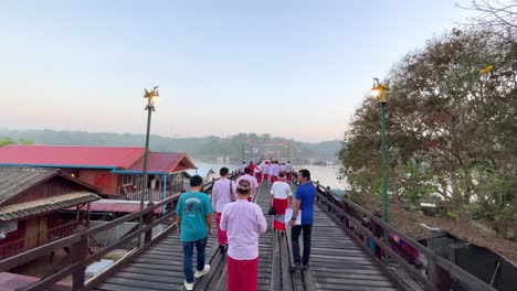 Establishing-slow-motion-of-tourists-passing-over-the-Mon-Bridge-in-Sangkhlaburi,-Thailand,-Static-reference-shot