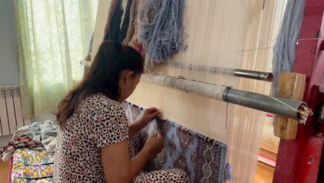 Una-Artesana-Vestida-Con-Ropa-Nacional-Hace-A-Mano-Una-Colorida-Alfombra-Tradicional-De-Lana,-Una-Alfombra-De-Pelo-Con-Adornos-Orientales